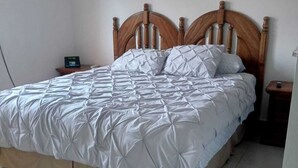 En säng med en trägavel, ett vitt, vadderat sängöverkast och ett nattduksbord med en lampa.