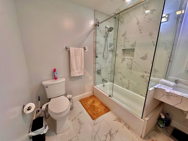 A bathroom with a toilet, a glass-enclosed shower, and a marble-tiled floor.