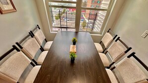 A conference table with six chairs, a small plant on the table, and a view of the street through large windows. - The Classy Suite: 2BR with Free Parking (Paterson)