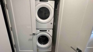 A compact laundry room with two stacked front-loading washing machines. - The Classy Suite: 2BR with Free Parking (Paterson)