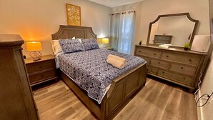 A bedroom with a wooden bed, two bedside tables with lamps, a dresser, and a mirror. - The Classy Suite: 2BR with Free Parking (Paterson)