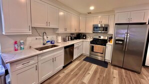 A modern kitchen with white cabinets, stainless steel appliances, and a wooden floor. - The Classy Suite: 2BR with Free Parking (Paterson)