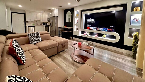 A modern living room with a sectional sofa, a coffee table, and a flat-screen TV mounted on the wall. - The Comfy Suite: 1BR with Free Parking (Paterson)