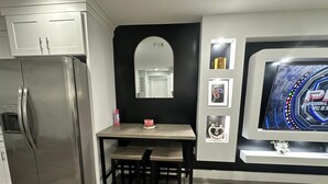 A kitchen with a stainless steel refrigerator, a wooden dining table with chairs, a black accent wall, and a framed picture above the table. - The Comfy Suite: 1BR with Free Parking (Paterson)