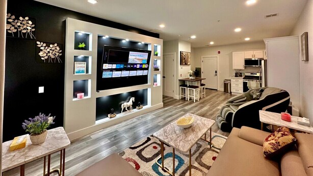 A modern living room with a flat-screen TV, a sofa, a coffee table, and a dining area with chairs. - The Stylish Spot: 1BR with Free Parking (Paterson)