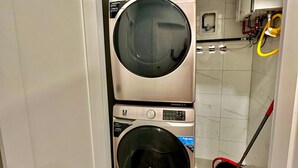 A compact laundry room with two stacked front-loading washing machines and a red mop in the corner. - The Stylish Spot: 1BR with Free Parking (Paterson)