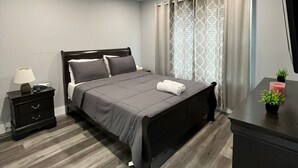 A modern bedroom with a bed, nightstand, and dresser. - The Lovely Suite: 1BR close to NYC (Paterson)