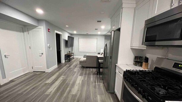 A modern kitchen with a gas stove, microwave, and refrigerator. There is a dining area with a table and chairs. - The Lovely Suite: 1BR close to NYC (Paterson)