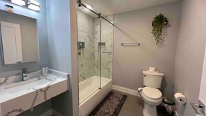 A modern bathroom with a glass-enclosed shower, a white toilet, and a sink with a marble countertop. - The Lovely Suite: 1BR close to NYC (Paterson)