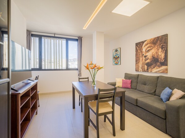 A modern living room with a sofa, a dining table with chairs, a TV, and artwork on the wall.