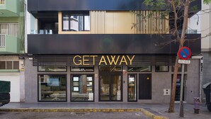 A modern building with a 'GETAWAY' sign, featuring a glass entrance and a tree in front.