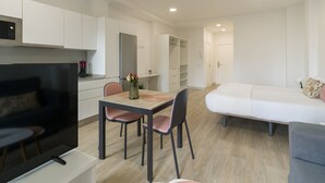 A modern, well-lit room with a dining area, a flat-screen TV, a sofa, and a bed.