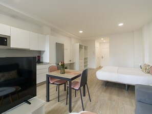 A modern, well-lit room with a dining area, a flat-screen TV, a sofa, and a bed.