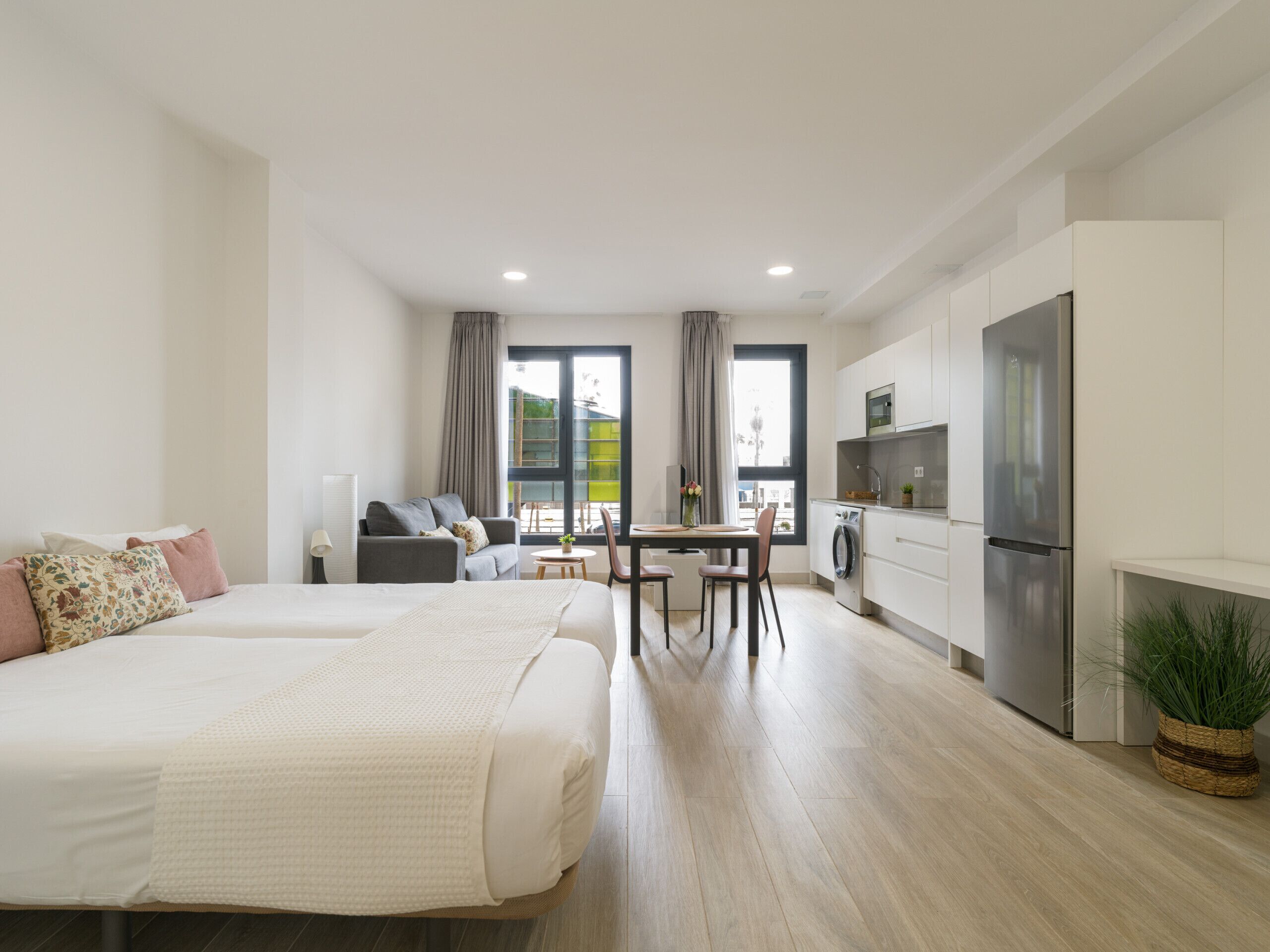 A modern apartment with a large bed, a dining area, a kitchen, and a view of the outdoors.