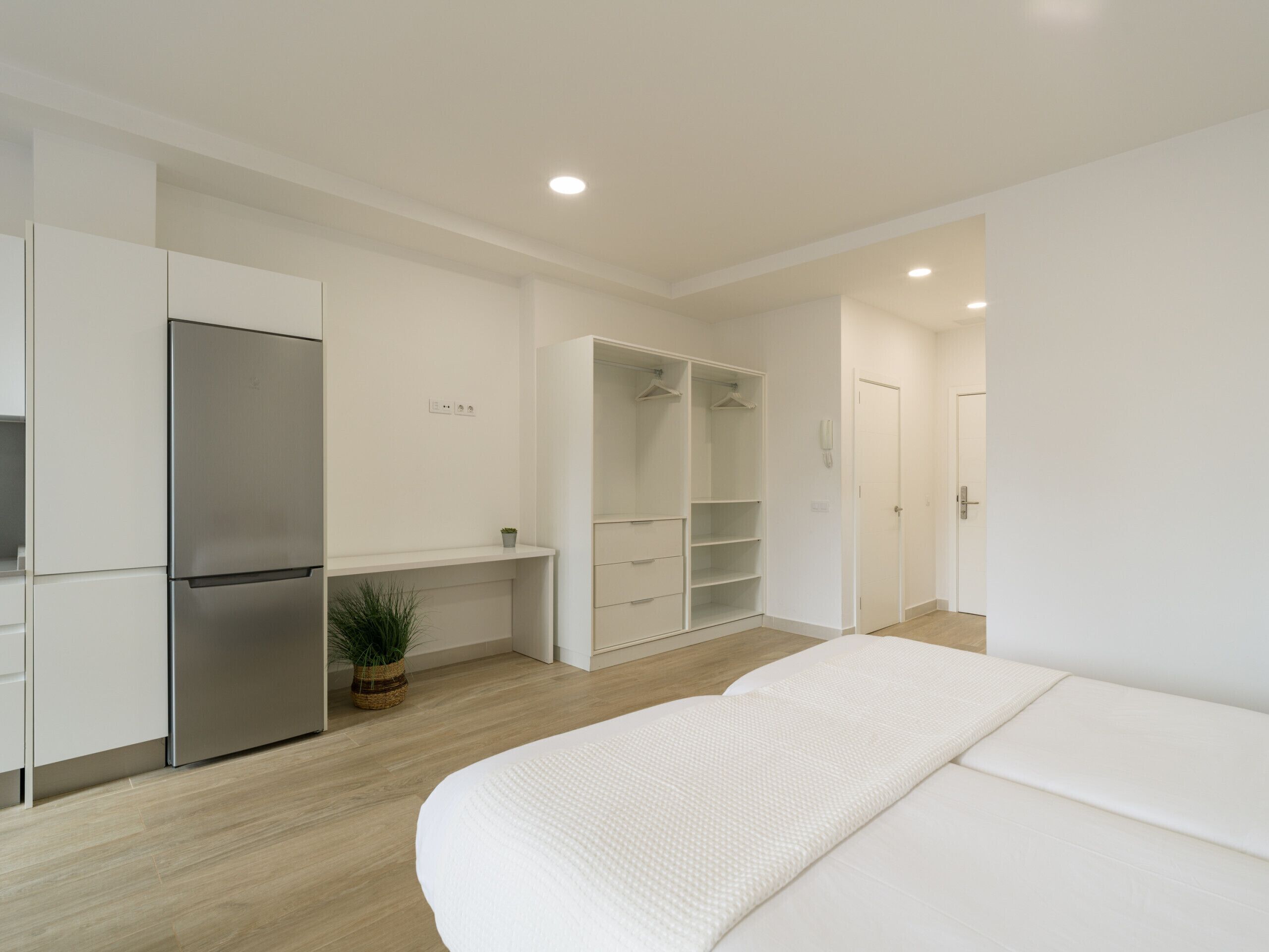 Ein modernes, minimalistisches Schlafzimmer mit einem großen Bett, einem eingebauten Kleiderschrank und einer Küchenzeile inklusive Kühlschrank.