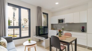 A modern apartment with a living area, a dining table, a kitchen, and large windows.