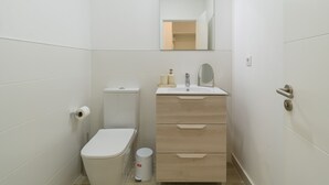 A small, white bathroom with a toilet, sink, mirror, and a trash can.