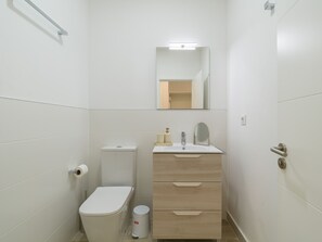 A small, white bathroom with a toilet, sink, mirror, and a trash can.