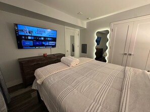 A bedroom with a large bed, a dresser, a TV mounted on the wall, and a wardrobe. - The Chic Suite: 1BR with Luxe Amenities (Paterson)