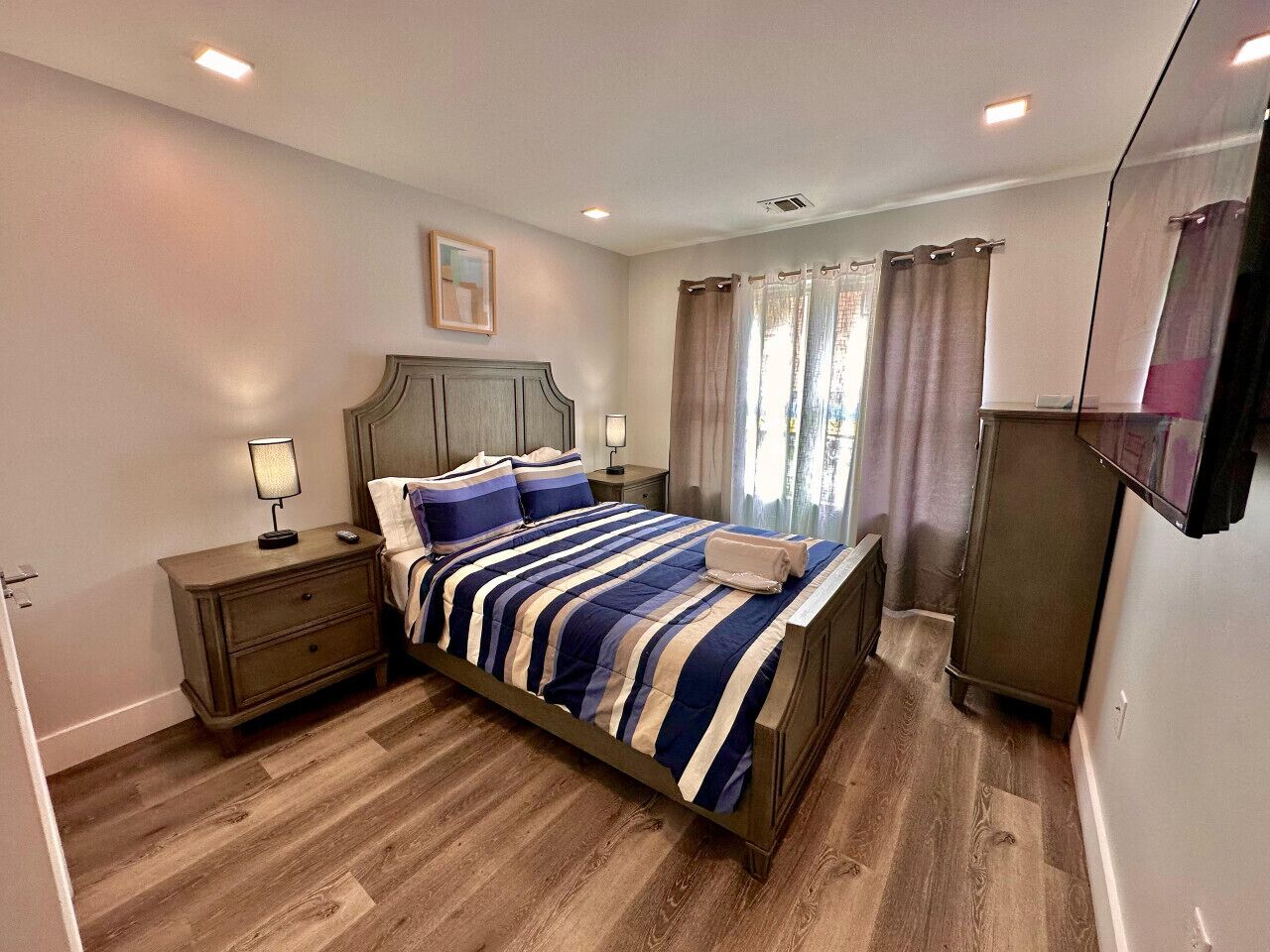 A bedroom with a bed, nightstands, a dresser, and a painting on the wall.