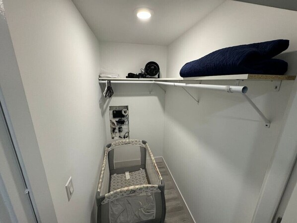A narrow hallway with a crib, a shelf with a blanket, and a wall-mounted fan.