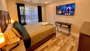 Habitación de hotel con una cama, un televisor montado en la pared, una mesita de noche con lámpara y suelo de madera.