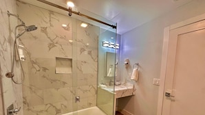 Un baño moderno con ducha envuelta en vidrio, una bañera independiente y un tocador con espejo.