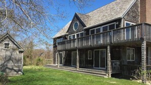 Een houten huis met twee verdiepingen, een balkon, een klein tuinhuisje en een gazon.