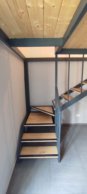 Una escalera con escalones de madera y barandillas de metal que sube a un piso superior.