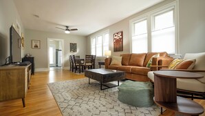 A spacious living room with a brown leather sofa, a wooden coffee table, and a dining area with chairs and a table. - Charming 2-bedroom house with WiFi, AC in brilliant Geneva (Geneva)