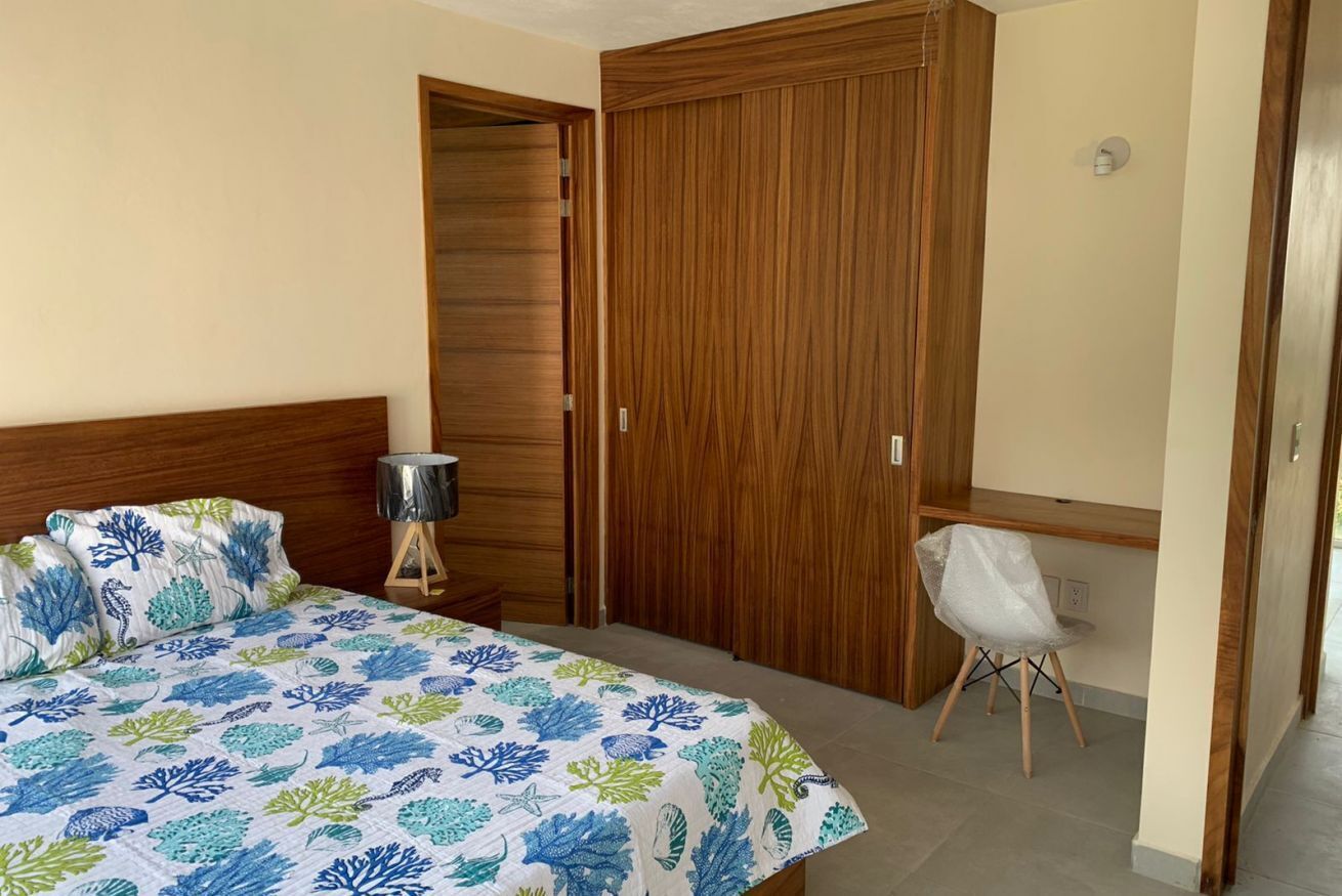 A bedroom with a bed, a wooden wardrobe, a desk, and a chair.