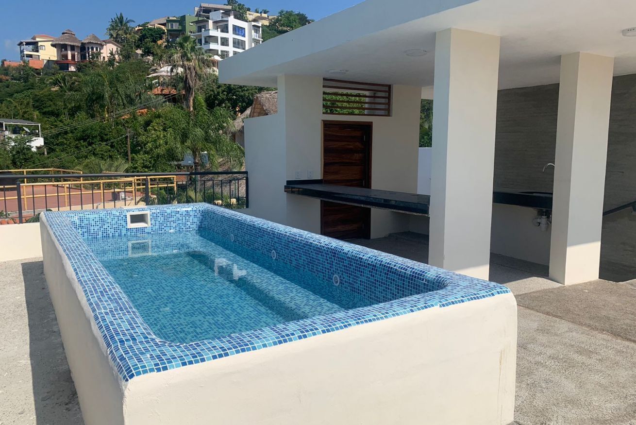 A rectangular swimming pool with blue mosaic tiles, surrounded by a white pool deck.