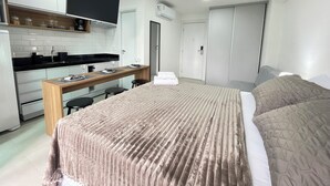 A compact hotel room with a kitchenette, a bed with a beige duvet, and a wardrobe. - RN Studio Premium 103 - Vista Mar (Maceió)