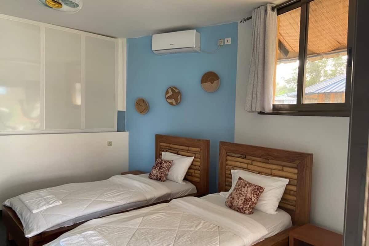 A room with two wooden beds, a ceiling fan, an air conditioning unit, and a window with a view of the outside.