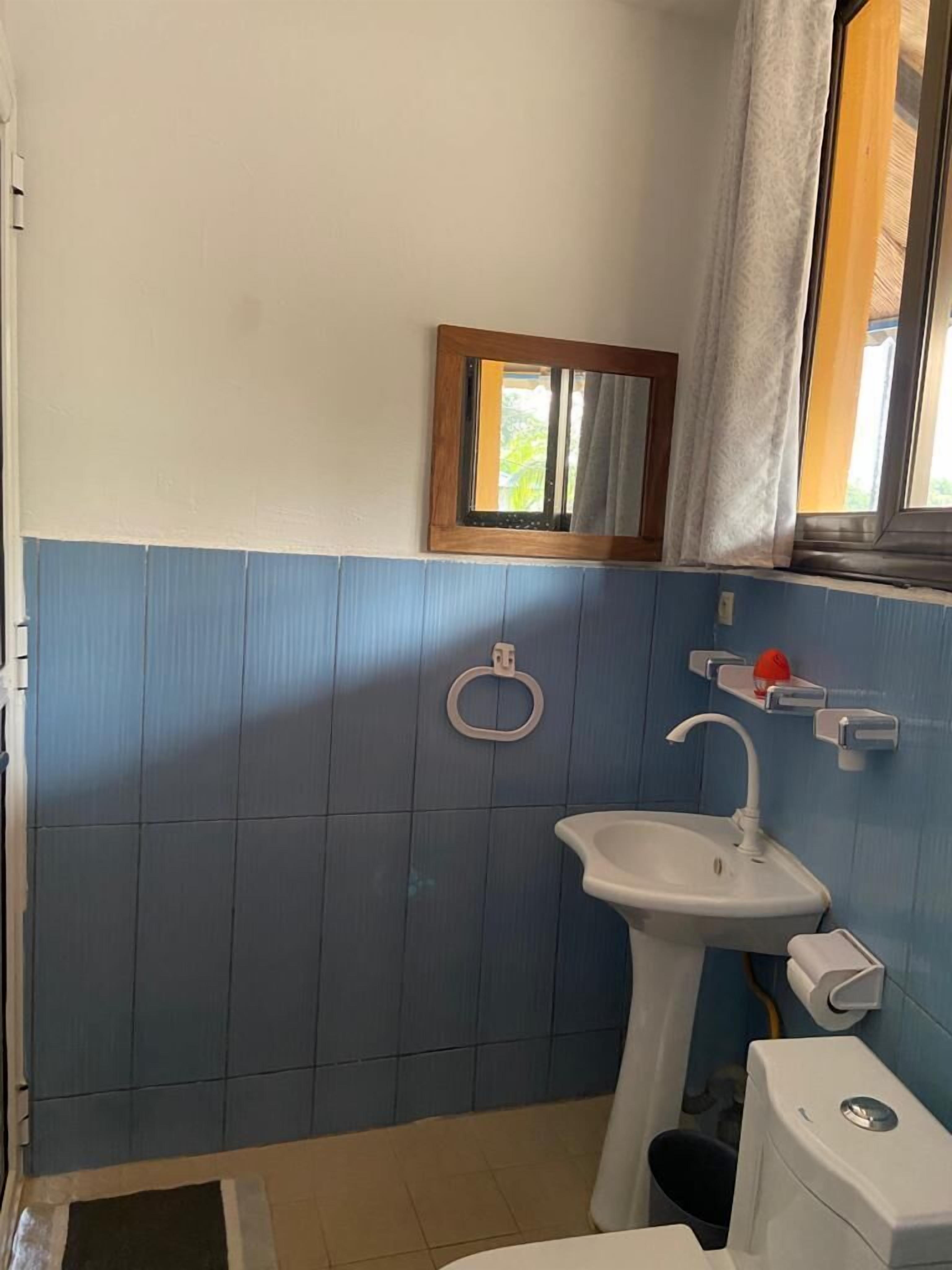 Un baño con lavamanos, inodoro y una pequeña ventana con espejo.