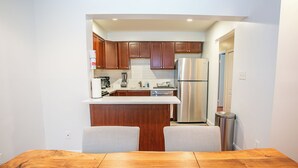 A compact kitchen with wooden cabinets, a stainless steel refrigerator, and a small island with seating. - Cozy 3 Bedroom/Great Location (Arlington)