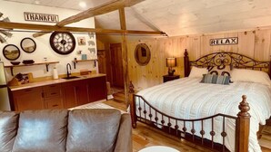 A cozy bedroom with a wooden ceiling fan, a large bed with a headboard, a sofa, a small round table, and a wall clock. - Couples Retreat: The HayLoft-  Rustic Escape For 2 (Oakland)