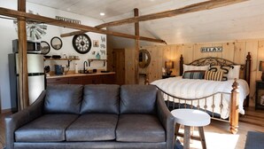 A cozy room with a bed, a sofa, a small table, and a kitchen area with a refrigerator and microwave. - Couples Retreat: The HayLoft-  Rustic Escape For 2 (Oakland)
