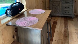 A wooden interior with a window, a table with placemats, a cabinet, and a mirror. - Couples Retreat: The HayLoft-  Rustic Escape For 2 (Oakland)