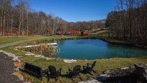 A pond with chairs and a dock, surrounded by trees and barns. - Couples Retreat: The HayLoft-  Rustic Escape For 2 (Oakland)