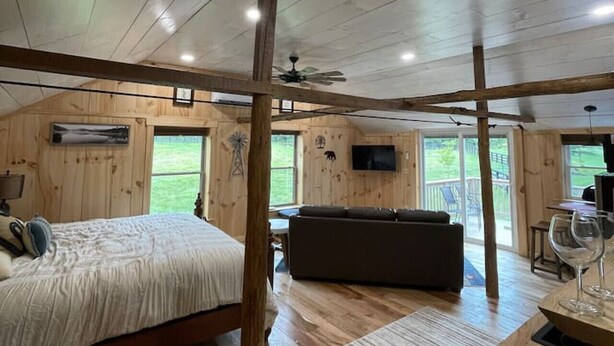 A spacious room with a large bed, a sofa, and a dining table. There are wooden walls and a ceiling fan. - Couples Retreat: The HayLoft-  Rustic Escape For 2 (Oakland)