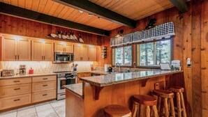 A wooden cabin-style kitchen with a large island, bar stools, and a window overlooking the forest.