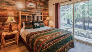 A wooden-paneled bedroom with a large bed, two bedside lamps, and a view of the outdoors.