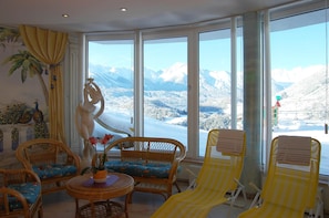 A room with large windows, wicker furniture, and a statue. - Apartment in Wald Near Hochzeiger Ski Area (Arzl im Piztal)