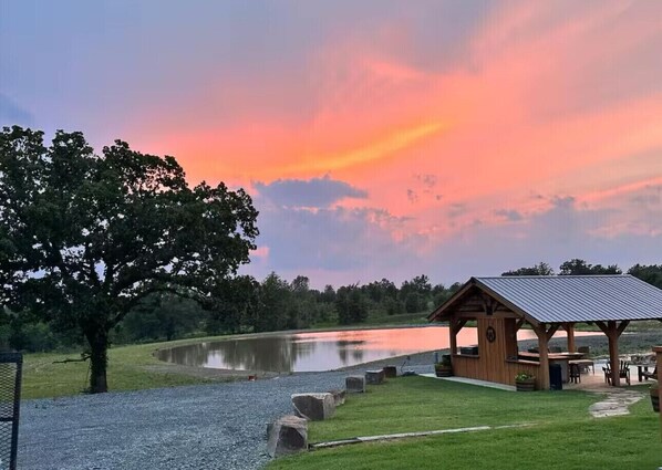 Enjoy serene lakeside gatherings in this tranquil outdoor space, featuring a pavilion with a metal roof and a shaded lawn.
