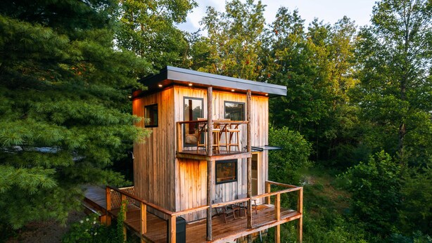 Een houten chalet met een balkon en terras, omgeven door een dicht bos.