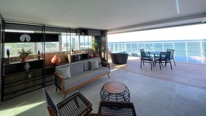 A modern living room with a sofa, chairs, and a dining area with a view of the ocean. - RN Studio Premium 412 - Frente Mar (Maceió)