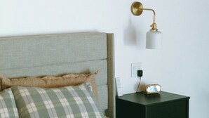 A bedroom with a bed, a nightstand, a lamp, and a wall socket. - Cozy Cabin Getaway (St. Ignace)