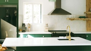 A modern kitchen with green cabinets, a white countertop, a central island with stools, a stove, and a hanging light fixture. - Cozy Cabin Getaway (St. Ignace)