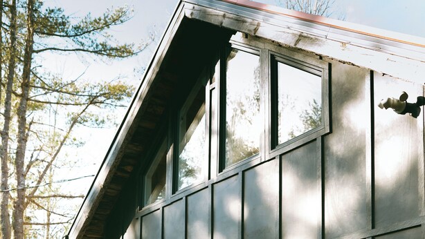 A modern two-story building with large windows, a wooden deck, and a small potted plant. - Cozy Cabin Getaway (St. Ignace)
